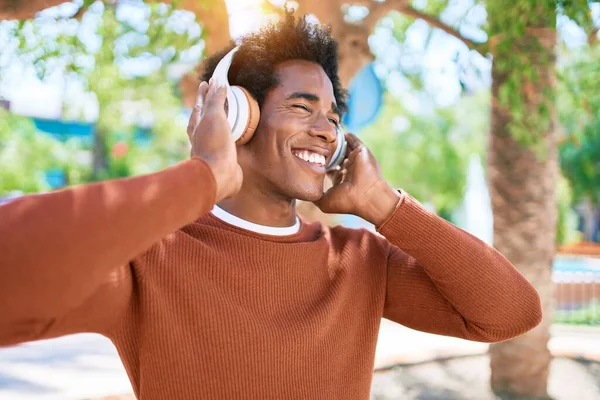 年轻英俊的非洲裔美国男人用耳机听音乐 站在街上 脸上挂着笑容 — 图库照片