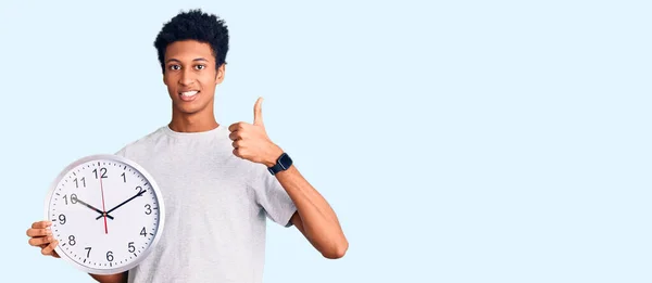 Joven Afroamericano Hombre Sosteniendo Gran Reloj Sonriendo Feliz Positivo Pulgar —  Fotos de Stock