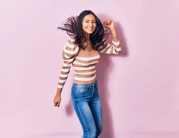 Young beautiful latin woman wearing casual clothes smiling happy. Jumping with smile on face over isolated pink background