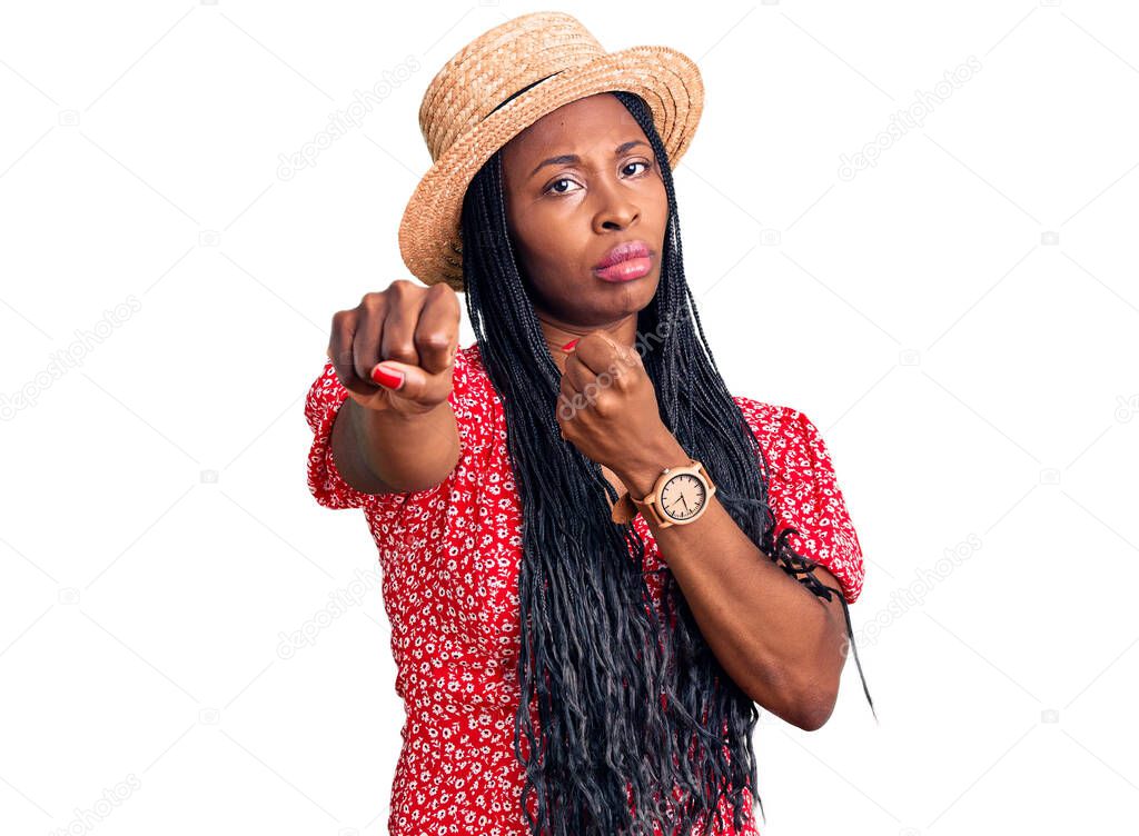 Young african american woman wearing summer hat punching fist to fight, aggressive and angry attack, threat and violence 