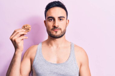 Sakallı, kolsuz tişörtlü, çikolatalı kurabiye yiyen, düşünceli, ayık bakışlı, kendine güvenen genç yakışıklı bir adam.