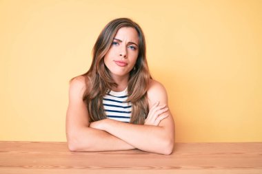 Masada rahat kıyafetler giyen, kuşkucu ve gergin, yüzünde çapraz kollarla tasvip etmeyen güzel, beyaz bir kadın. negatif kişi. 