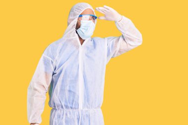 Koronavirüs üniforması ve tıbbi maske takan genç İspanyol adam çok mutlu ve gülümsüyor. arama kavramı. 