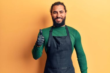 Berber önlüğü giymiş genç Arap adam mutlu ve pozitif gülümsüyor, başparmağıyla mükemmel ve onay işareti yapıyor. 