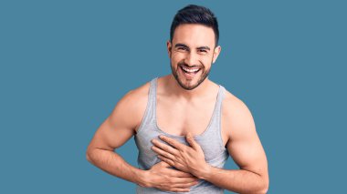 Mayo ve kolsuz tişört giyen genç yakışıklı adam gülümseyerek kahkahalarla gülüyor.. 