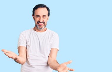 Orta yaşlı yakışıklı bir adam gündelik tişörtler giyiyor. Neşeli gülümsüyor ve kollarını açıyor. Hoş geldin, olumlu ve kendinden emin selamlar. 