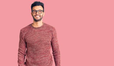 Kışlık süveter giyen ve yüzünde mutlu ve havalı bir gülümsemeyle gözlük takan genç, yakışıklı İspanyol adam. şanslı kişi. 