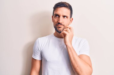 İzole edilmiş beyaz arka plan üzerinde duran sıradan tişört giyen genç ve yakışıklı bir adam parmak çenesinde ve yukarı bakarak şüphe üzerine yoğunlaşmıştı.