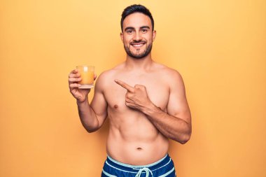 Tatilde sakallı, mayo giyen, bir bardak portakal suyu içen, mutlu, eli ve parmağı olan genç bir adam.