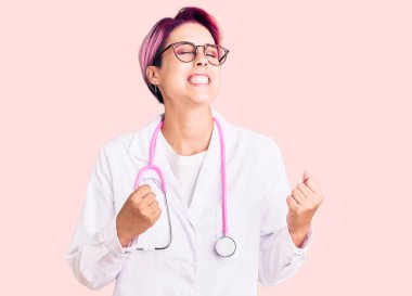 Pembe saçlı, doktor üniforması giyen genç ve güzel bir kadın. Başarılı olacağı için heyecanlı. Kolları havada ve gözleri kapalı zaferi kutluyor. Kazanan konsept. 