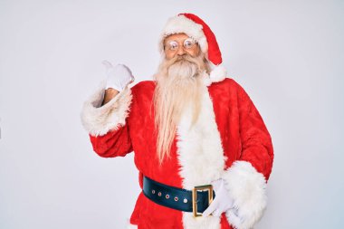 Gri saçlı, uzun sakallı, Noel Baba kostümü giyen mutlu yüzüyle gülümseyen ve baş parmağıyla yüzünü gösteren yaşlı bir adam.. 