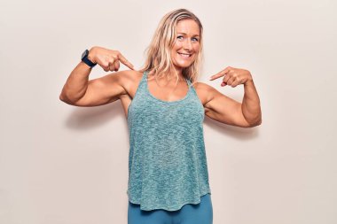 Orta yaşlı, beyaz giyimli, spor giyinen, kendine güvenen, kendini gururlu ve mutlu gösteren sarışın bir kadın.. 