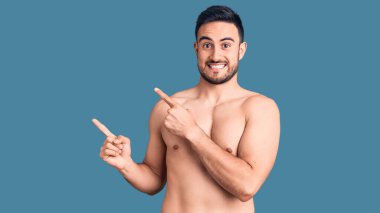 Mayo giyen genç yakışıklı adam gülümsüyor ve kameraya bakıyor. İki eliyle ve parmaklarıyla kenarı işaret ediyor.. 