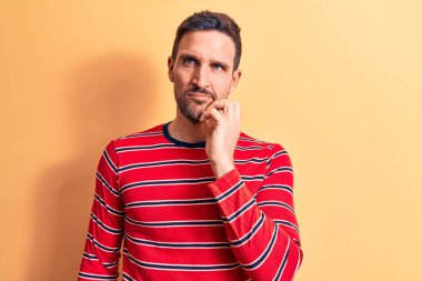 Sıradan çizgili tişört giyen genç yakışıklı adam izole edilmiş sarı arka planda dikiliyor şüphe üzerine yoğunlaşmıştı.