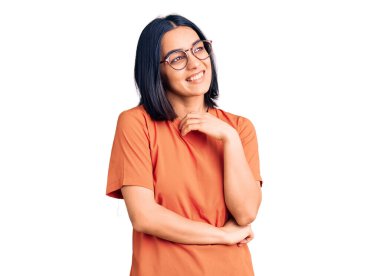 Gündelik kıyafetler giyen genç, güzel Latin bir kadın yüzünde gülümsemeyle yan yana bakıyor, doğal bir ifade. Kendinden emin gülen. 