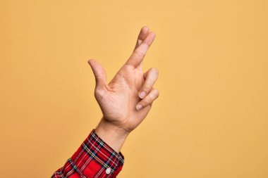 Kafkas genci parmaklarını izole edilmiş sarı arka plan üzerinde gösteriyor. Parmaklarını çapraz yapıyor, batıl inançlar ve şanslı bir jest, şanslı ve umut dolu bir ifade.
