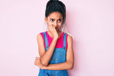 Pembe arka planda günlük kıyafetler giyen Afro-Amerikalı genç bir kız. Elleri ağızdan tırnak yerken gergin ve stresli görünüyor. anksiyete. 