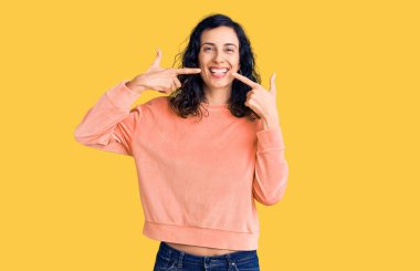 Gündelik kıyafetler giyen, neşeli gülümseyen, parmaklarıyla ve ağzıyla işaret eden genç, güzel İspanyol bir kadın. diş sağlığı kavramı. 