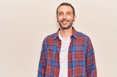 Gündelik kıyafetler giyen yakışıklı genç adam pozitif ve mutlu görünüyor. Duruyor ve gülümsüyor. Kendine güvenen bir gülümsemeyle dişlerini gösteriyor. 