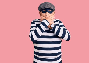 Hırsız maskesi takan ve tişört giyen son sınıf yakışıklı adam yanlışlıkla ağzı ellerle kapatmış. gizli kavram. 