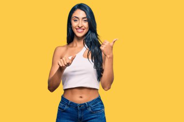 Güzel İspanyol kadın, gündelik kıyafetler giyip arkasını işaret ediyor. Elleri havada, kendinden emin gülümsüyor. 