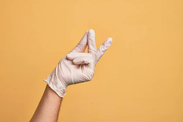 Mão Homem Jovem Caucasiano Com Luva Médica Sobre Fundo Amarelo — Fotografia de Stock