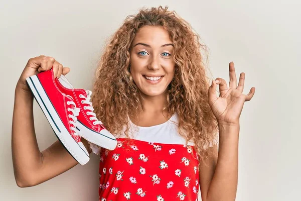 Hermosa Chica Adolescente Caucásica Sosteniendo Zapatos Casuales Rojos Haciendo Signo —  Fotos de Stock