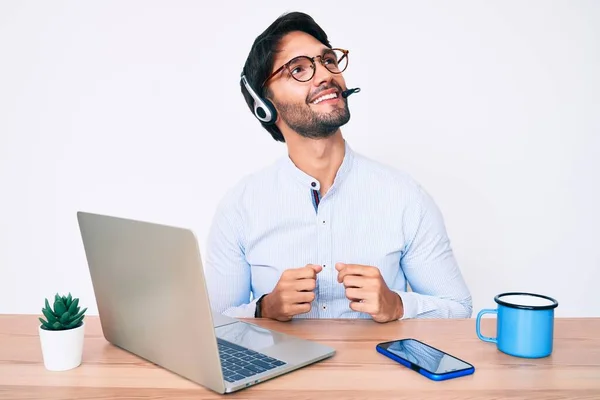 Handsome hispanic man working at the office wearing operator headset looking to side, relax profile pose with natural face and confident smile.