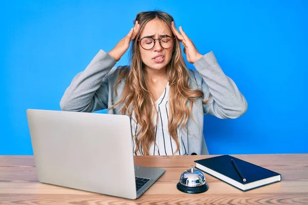 Otelin resepsiyonunda eli başının üstünde oturan genç, güzel sarışın kadın, stresten baş ağrısı çekiyor. migren ağrısı. 