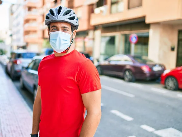 若い配達人は自転車のヘルメットとコロナウイルス保護医療マスクを着て街の通りに立っている — ストック写真