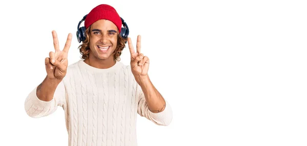 Kulaklıkla Müzik Dinleyen Gülümseyen Parmaklarını Zafer Işareti Yaparken Gösteren Genç — Stok fotoğraf