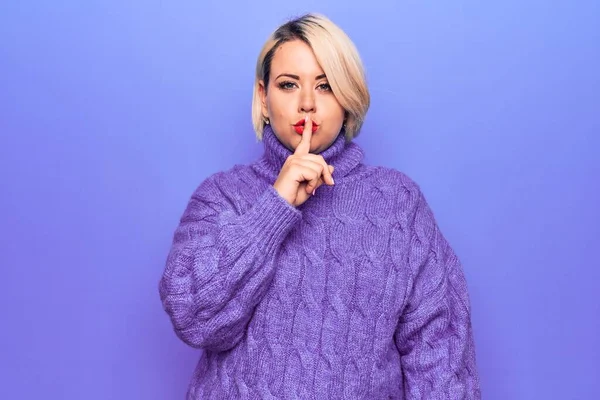 Güzel sarışın ve cüsseli bir kadın mor arka planda balıkçı yaka kazak giyip sessiz olmak istiyor. Sessizlik ve gizli konsept.