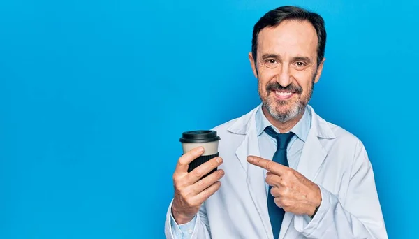 中年ハンサムな医師男身に着けていますコート飲みカップのテイクアウトコーヒー笑顔幸せなポインティングとともに手と指 — ストック写真