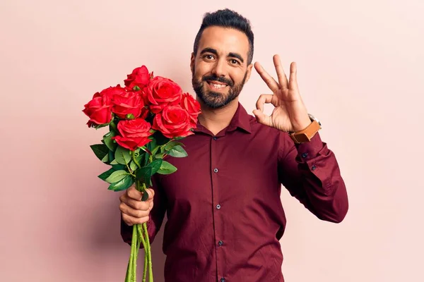 Homem Hispânico Jovem Segurando Flores Fazendo Sinal Com Dedos Sorrindo — Fotografia de Stock