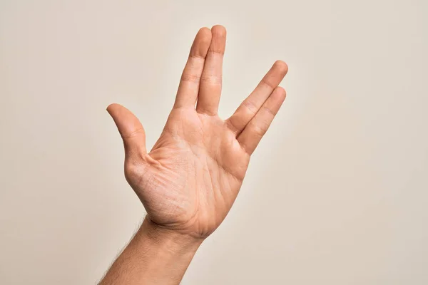 Hand of caucasian young man showing fingers over isolated white background greeting doing Vulcan salute, showing hand palm and fingers, freak culture