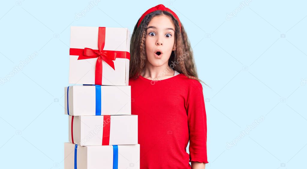 Cute hispanic child girl holding gift scared and amazed with open mouth for surprise, disbelief face 
