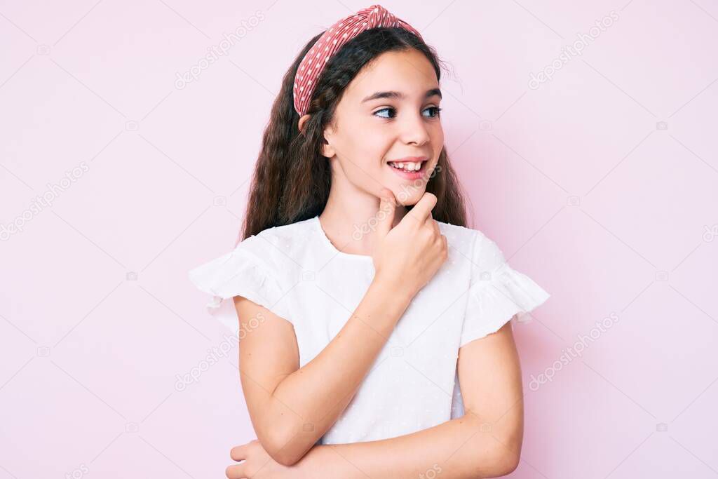 Cute hispanic child girl wearing casual clothes and diadem with hand on chin thinking about question, pensive expression. smiling with thoughtful face. doubt concept. 