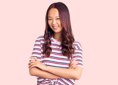 Genç, güzel, Çinli, sıradan kıyafetler giyen mutlu yüzlü, kollarını kavuşturup kameraya bakan bir kız. pozitif kişi. 