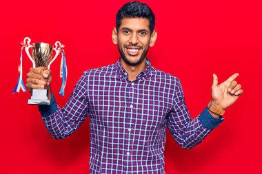 Elinde kupa tutan genç latin adam gülümsüyor mutlu bir şekilde elini ve parmağını kenarda gösteriyor. 