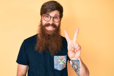 Uzun sakallı, sıradan kıyafetler ve gözlük takan, kameraya gülümseyen ve zafer işareti yapan yakışıklı kızıl saçlı genç adam. İki numara.. 