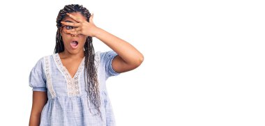 Saçları gündelik yaz kıyafetleri ve gözlükleriyle örülü, yüzü ve gözlerini kapayarak utangaç bir ifadeyle parmaklarının arasından bakan Afro-Amerikalı genç bir kadın.. 