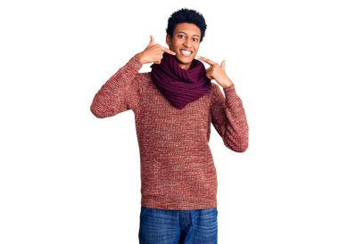 Genç Afro-Amerikan adam, günlük kışlık süveter ve atkı giyerek neşeli bir şekilde gülümseyerek parmaklarını ve ağzını işaret ediyor. diş sağlığı kavramı. 
