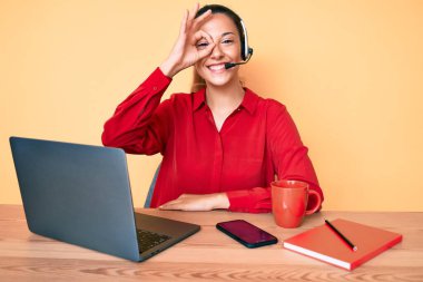 Çağrı merkezinde operatör kulaklığı takan genç esmer kadın gülümsüyor. 