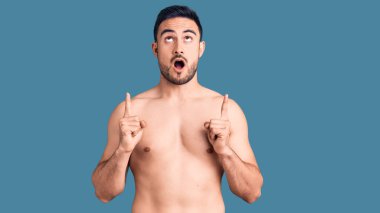 Mayo giyen genç ve yakışıklı adam şaşırmış ve şaşırmış görünüyor ve parmaklarıyla işaret ediyor ve kollarını kaldırıyor.. 