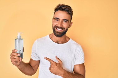 Genç İspanyol adam el dezenfektanı jeli kullanıyor gülümsüyor mutlu bir şekilde eli ve parmağı işaret ediyor. 