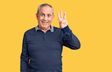 Kıdemli yakışıklı adam gündelik polo giyip üç numaralı parmaklarıyla işaret ederken kendinden emin ve mutlu gülümsüyor.. 