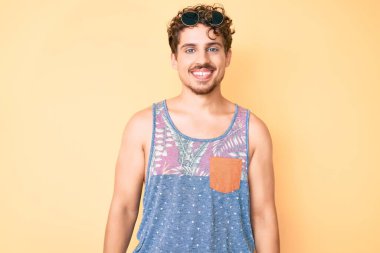 Kıvırcık saçlı, sıradan giyinen, kolsuz gömlekli, yüzünde mutlu ve havalı bir gülümseme olan beyaz bir genç. şanslı kişi. 