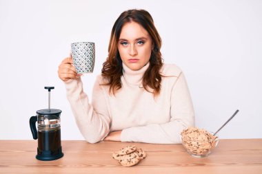 Genç, güzel, beyaz bir kadın masada oturmuş kahvaltı yapıyor. Duruşunu ve ayık ifadesini düşünüyor. Kendine güveniyor gibi görünüyor. 