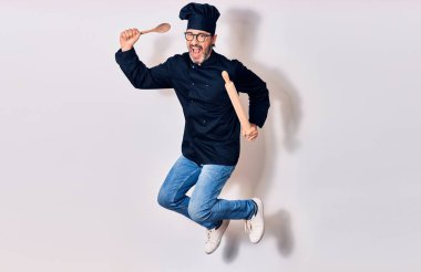 Orta yaşlı, yakışıklı, gözlüklü ve aşçı üniformalı mutlu bir adam. Yüzünde tebessümle hoplayarak yoğurucu ve kaşıkla soyutlanmış beyaz arka plan