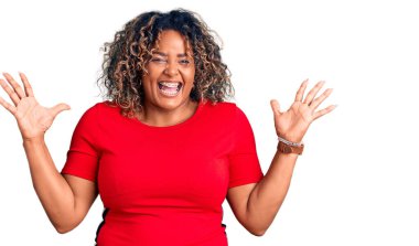 Genç Afro-Amerikan artı cüsseli kadın gündelik kıyafetler giyip zaferi mutlu bir gülümsemeyle kutluyor ve ellerini kaldırarak kazanan yüz ifadesi sergiliyor. 